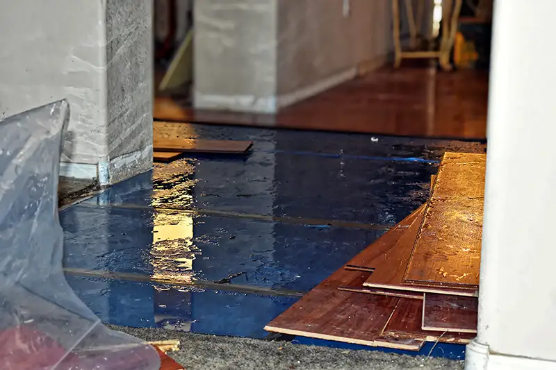 Water-damaged flooring with standing water pooling on the surface, exposing partially installed wooden planks. Prompt restoration services are essential to prevent further damage and reduce repair costs. Call BCC Restoration for fast emergency response.